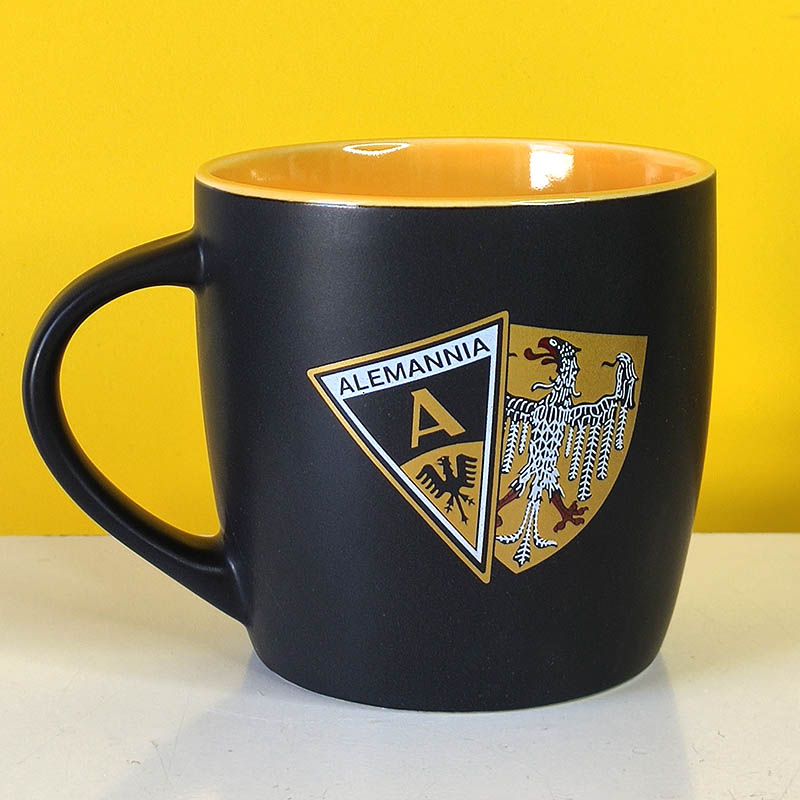 Black mug with a yellow interior featuring the Alemannia crest on the side of the cup.
