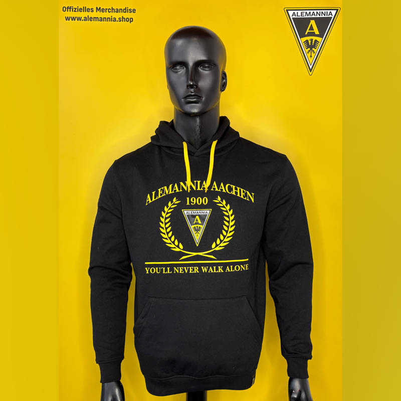 Mannequin wearing a black hoodie with yellow Alemannia Aachen crest and laurel emblem on a bright yellow background; includes slogan 'YOU’LL NEVER WALK ALONE'.