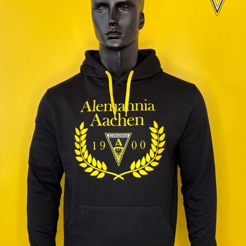 Black Alemannia Aachen hoodie on a mannequin against a bright yellow backdrop; features yellow club crest and 'Alemannia Aachen' text on the chest.
