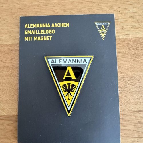 Dark booklet displaying Alemannia Aachen enamel logo magnet with shield emblem and yellow text on a black cover