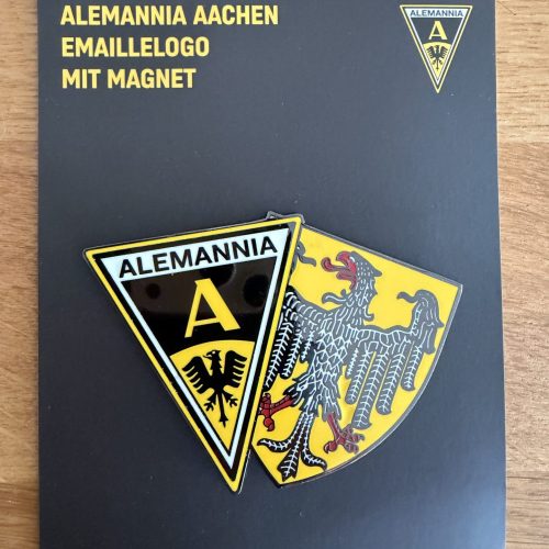 Dark slate booklet cover with yellow German text about Alemannia Aachen enamel logo magnets and crest emblems attached nearby.