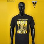 Mannequin wearing a black T-shirt with yellow 'Alemannia 1900 Aachen' logo on a bright yellow backdrop