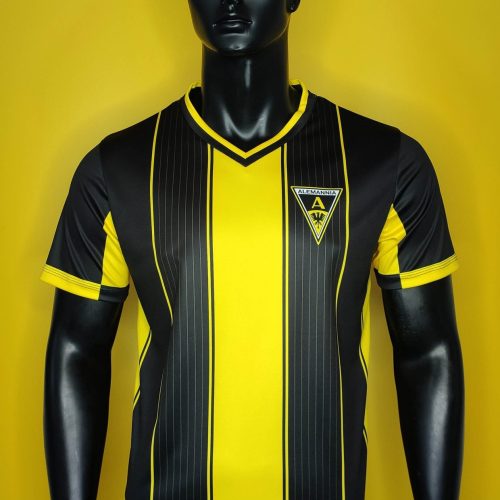 Black mannequin wearing a yellow and black striped soccer jersey with an Alemannia crest on the chest against a yellow background