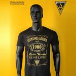 Black mannequin wearing a dark T-shirt with gold Alemannia Aachen graphics, yellow background with crest in top right and shop text top left