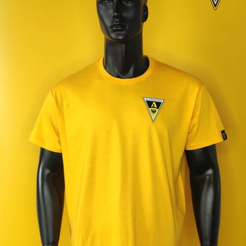 Black mannequin wearing a bright yellow T-shirt with the Alemannia logo on the chest, set against a yellow backdrop with a logo in the corner.
